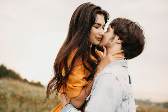 Close up of a lovely young couple embracing outdoor on a field. Charming young brunette embracing with closed eyes her boyfriend while he is kissing her.