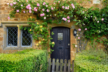Historic thatched cottage in Great Tew village with climbing rose on yellow cotswold stone...