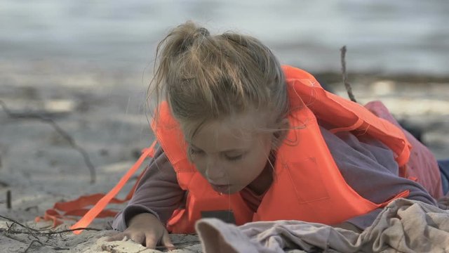 Little girl in life vest spitting water on sea coast, shipwreck survived victim