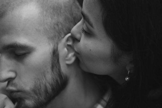 the concept of a romantic stroll. A girl kisses a guy in the ear. Black and white photo: caucasian man and Asian woman