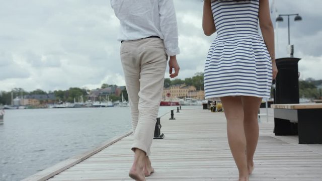 A young travelling couple walking barefoot on a wooden dock in Stockholm.