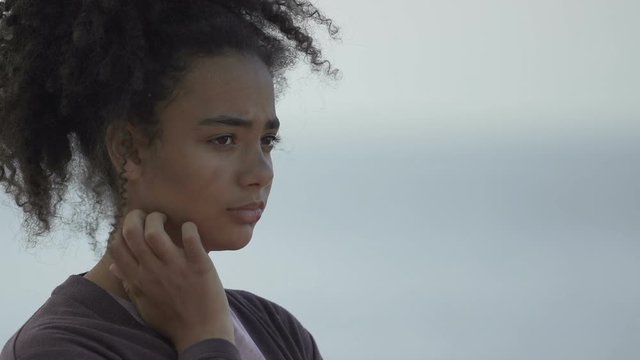 Depressed African-American teen girl standing alone, awkward age problems