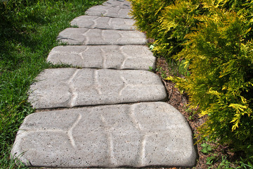 Grey wide path or trail of the embossed patterned shaped concrete slabs lying among green grass and...