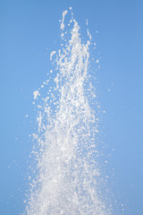 Naklejka na ściany i meble Spray of water fountain against the blue sky. Water splashes are out of focus.