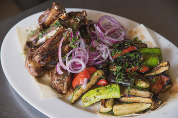 rack of lamb with grilled vegetables, decorated with sweet onion sweet onion on a white platter