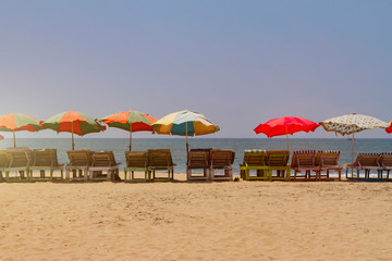 Row of covered wooden deck chairs with colorful umbrellas on the beach, toned with sunlight. Bright summer background. Holiday template.