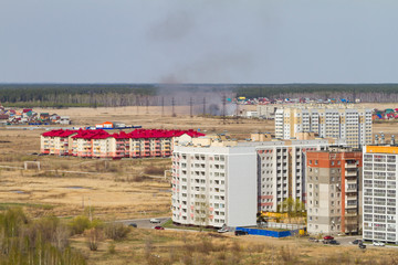 Dark smoke from burning dry yellow grass. Window view on apartment building. Summer time. Long shot.