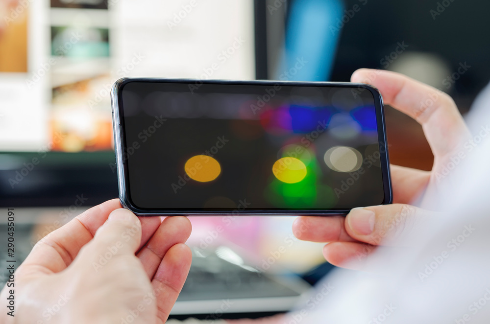 Poster closeup view man hand holding smartphone with bokeh image on screen.