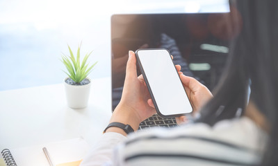 Closeup view young woman holding smartphone with blank screen while working with laptop.Closeup view young woman holding smartphone with blank screen while working with laptop