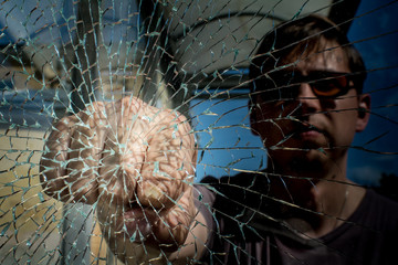 The man is on the street, behind the broken glass. The man presses his hand to the glass.