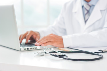Senior doctor at his office in hospital working close-up blurred using laptop typing