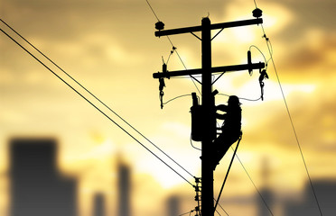 Silhouette electrician working maintenance equipment on electric pole in sunset background.