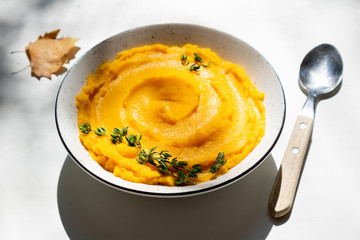 Autumn pumpkin puree in a bowl. Vegetarian autumn pumpkin cream soup with thyme on table with sunny beams. Autumnal tasty dinner or lunch