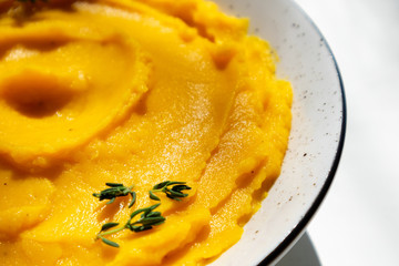 Autumn pumpkin puree in a bowl. Vegetarian autumn pumpkin cream soup with thyme on table with sunny beams. Autumnal tasty dinner or lunch