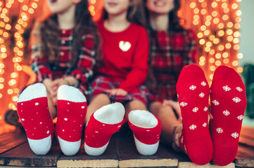 Feet wearing Christmas socks on wood floor. Happy family of three girls at home.