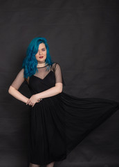 Fototapeta na wymiar People and fashion concept - Woman dressed in black dress and blue hair posing over black background