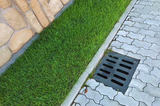 Plastic drain gutter, green grass lawn and stone pavement sidewalk.