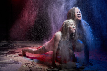 Two sisters in black studo with red and blue light during photoshoot with flour