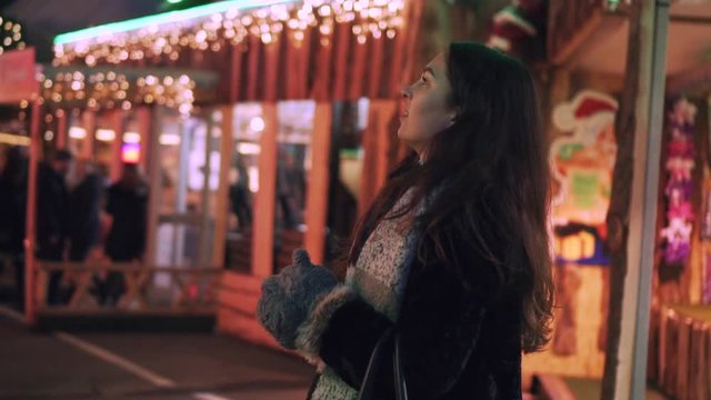 A beatiful woman on a christmas market looks at the lights in the distance while warming her hands in slow motion.