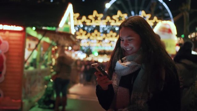 A young lady is texting and laughing at a christmas market in slow motion.