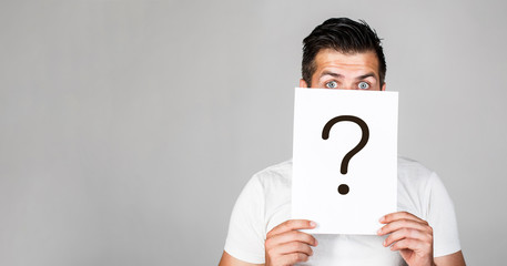 Portrait of man, peeking behind of interrogation symbol. Question mark, symbol. Pensive male. Man a question. Doubtful man holding Question Mark. Problems and solutions. Copy space