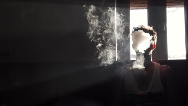 Man vaping in the darkness of a room.