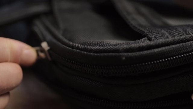 Hand pulling metal zip  to open black briefcase