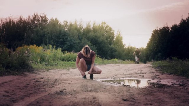 Woman stops to tie her shoes and gets splashed by a rude man on a bike.