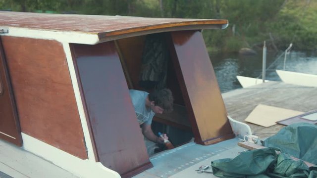 Young man painting wooden boat wheelhouse cabin