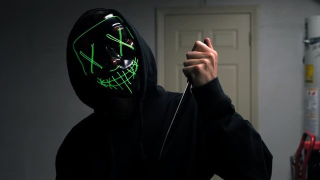 A scary slasher killer in a generic halloween horror mask pulling a knife on his murder victim.