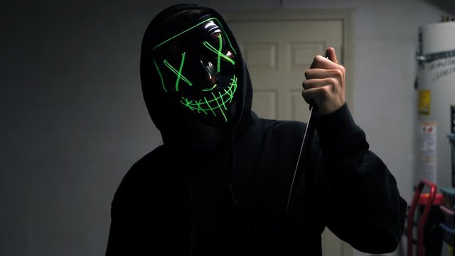 A frightening slasher killer in a generic anonymous halloween horror mask pulling a knife on his murder victim.