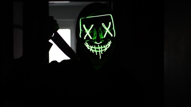 A terrifying killer in a generic halloween mask chasing a scared murder victim with a knife in slow motion.