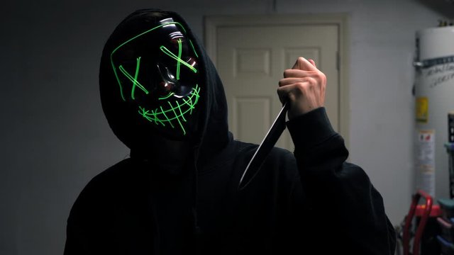 A scary slasher killer in a generic halloween horror mask pulling a knife on his murder victim.