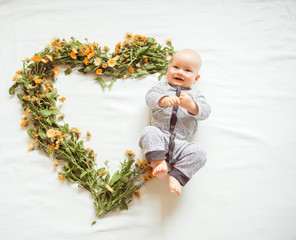 Smiling baby shapes heart with flowers on white background