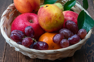 red grape berries and fresh fruits in a straw basket on a dark wooden background