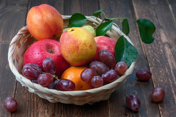 Fototapeta na wymiar red grape berries and fresh fruits in a straw basket on a dark wooden background
