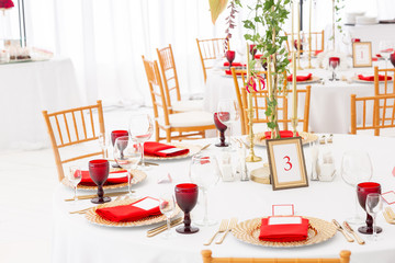 Table setting red napkins and glasses, gold plates. Interior of a wedding tent decoration ready for guests. Decor flowers. Red theme