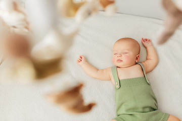 Little baby girl sleeps on a bed in a green suit playmobile revolves over her.