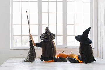 Girls in Halloween costumes with broom sitting near window