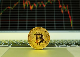 A gold bitcoin puts on a touch pad of a notebook computer with a stock graph in the background