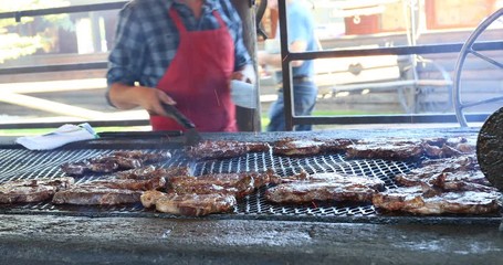 BBQ cooking steaks on large outdoor grill. Outdoor family gathering and picnic. Hamburgers, steak and chicken cooked over fire. Outdoor recreation and meal time for lunch or dinner.