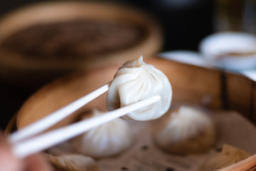 Fototapeta na wymiar Close up white chopsticks holding dim sum Ha gow over wooden basket. (traditional Cantonese dumpling) chinese food.