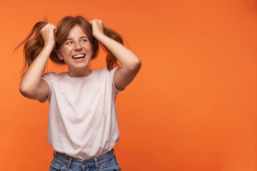 Happy young lovely woman with red hair standing over orange background in casual wear, looking...