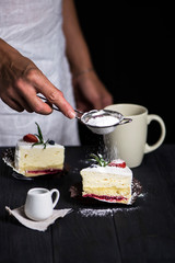 chef's hand sprinkles icing sugar cake with white cream and strawberries on a dark background