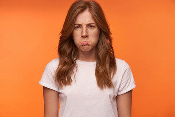 Studio close-up of charming offended young female posing over orange background, pouting and...