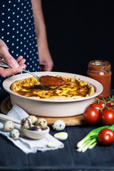 chef's hand cook tasty meat pie with carrots, onions and cheese in a baking dish on a dark background
