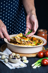 chef's hand cook tasty meat pie with carrots, onions and cheese in a baking dish on a dark background