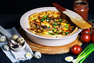 meat pie with carrots, onions and cheese in a baking dish on a dark background
