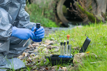 a worker in a protective suit takes samples of water and soil for contamination