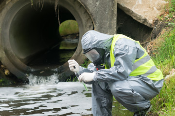 Fototapeta na wymiar a man in a protective suit takes a sample of water from the river after the release of chemical waste